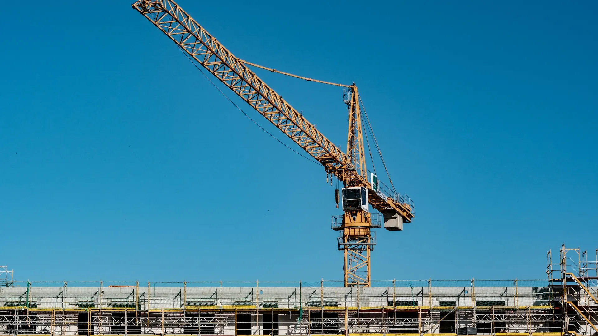 Grúa torre sobre edificio en construcción con andamios y cielo despejado